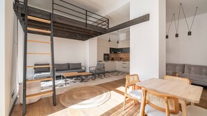 Um apartamento moderno no estilo loft com cama em mezzanine, área de refeições com mesa e cadeiras, cozinha e sala de estar com sofá e mesa de centro.