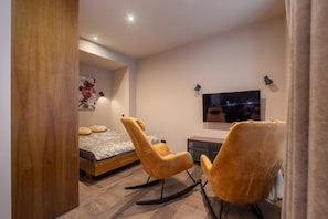 A modern bedroom with a bed, two rocking chairs, a TV, and a wooden door. - Stylish old town apartment (Rīga)