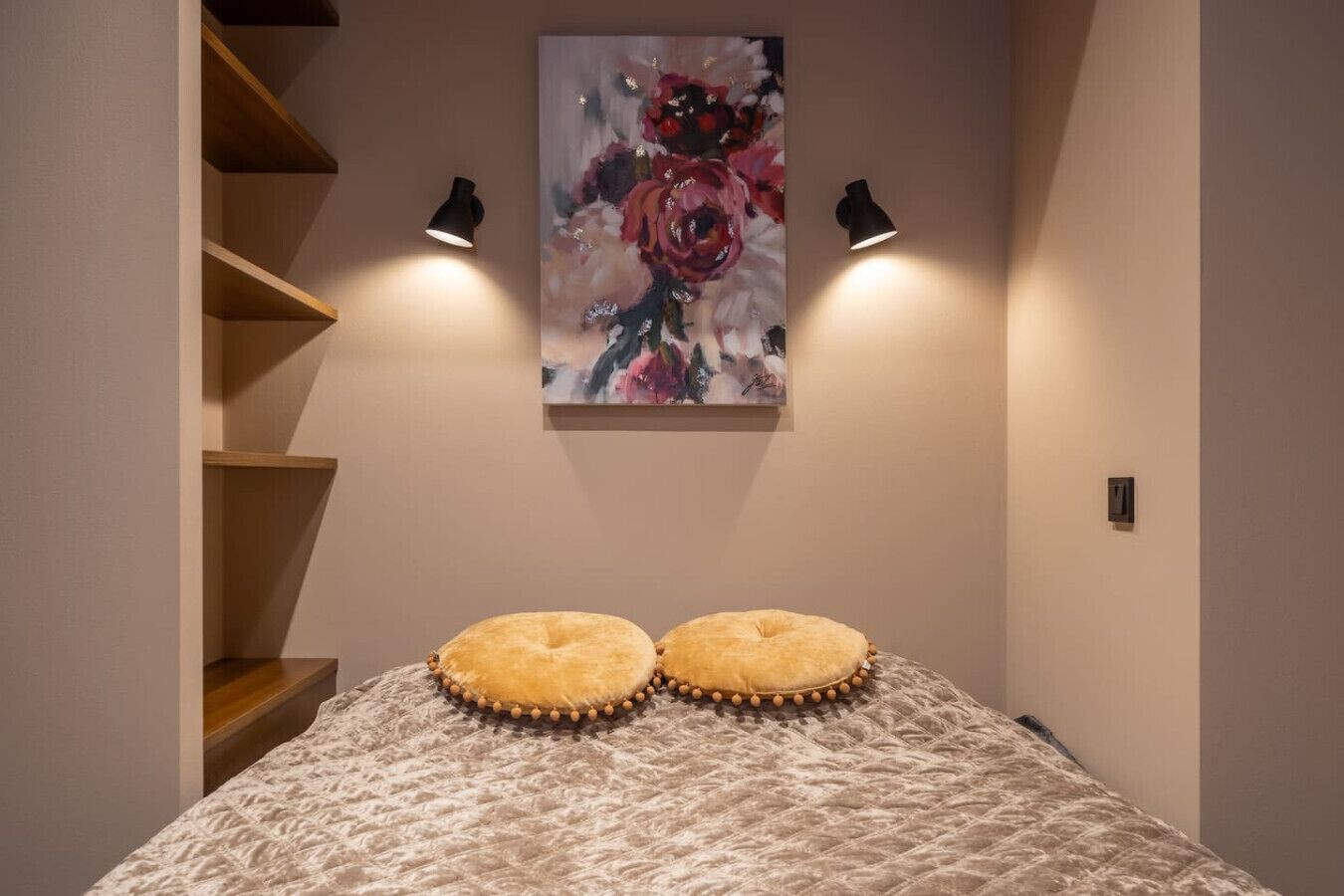 A bedroom with a bed, two pillows, a painting, and two wall-mounted lamps.