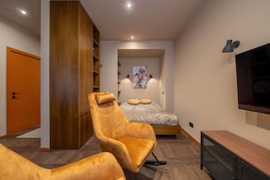 A modern bedroom with a large bed, a wooden wardrobe, a TV, and a plush armchair. - Stylish old town apartment (Rīga)