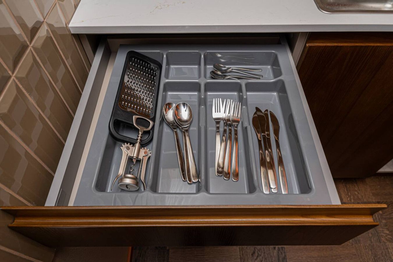 A drawer containing a grater, a corkscrew, a spoon, a fork, a knife, and a pair of chopsticks.