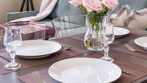 Une table à manger dressée avec des assiettes, des verres et un vase rempli de fleurs, avec un canapé et une lampe en arrière-plan.