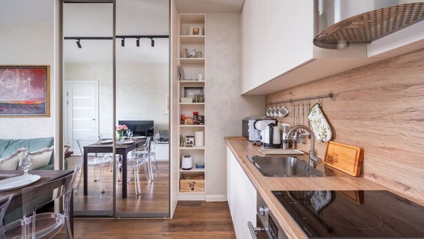 Une cuisine moderne dotée d’un plan de travail en bois, d’un évier en acier inoxydable et d’un four encastré. On y trouve également un coin repas avec une table et des chaises en verre, ainsi qu’une porte coulissante donnant sur une autre pièce.