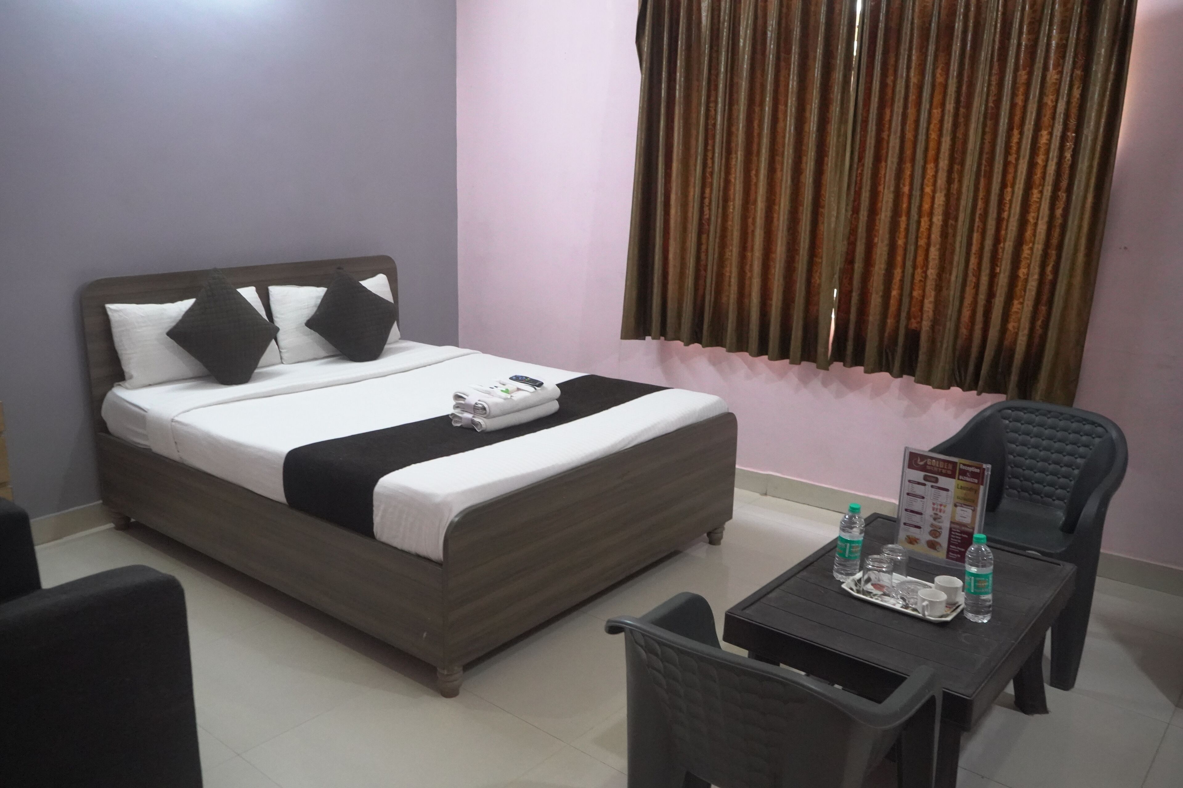 A neatly arranged hotel room with a bed, a small table with a tray of breakfast items, and a chair.
