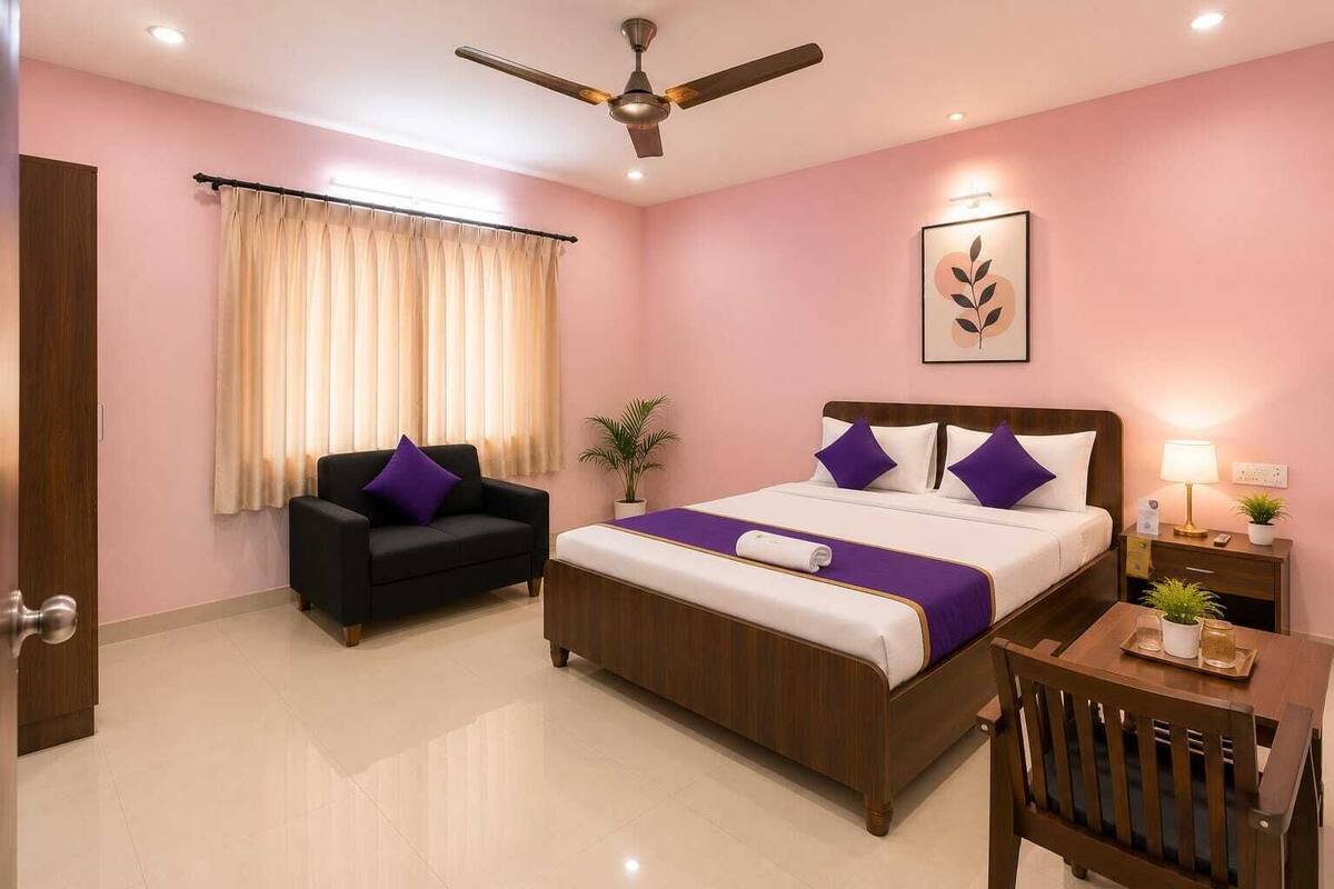 A hotel room with a bed, a chair, a desk, a ceiling fan, and a window with curtains.