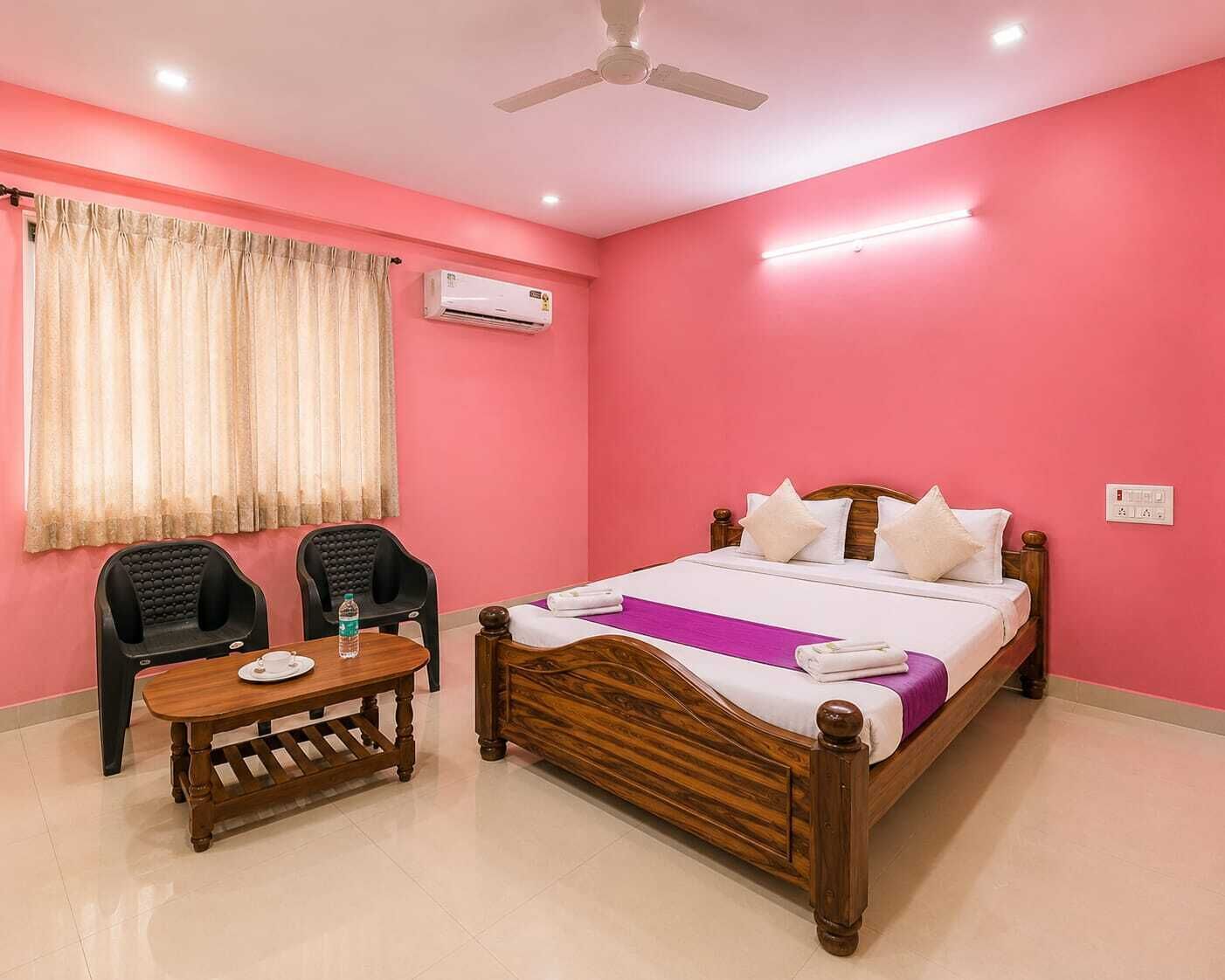 A bedroom with a bed, a bedside table, two chairs, a ceiling fan, and an air conditioning unit.