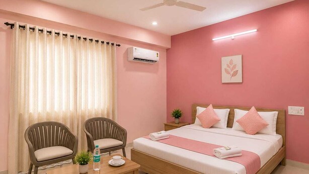 A bedroom with a bed, two chairs, a table, an air conditioner, and a ceiling fan.