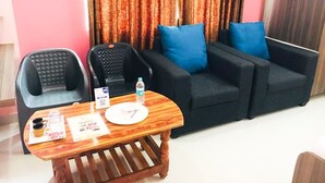 A living room with a black sofa, two blue cushions, a wooden coffee table, a black telephone, and a water bottle.
