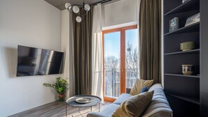Una sala de estar moderna con un sofá, una mesita redonda, un televisor de pantalla plana, una estantería y una ventana con cortinas.