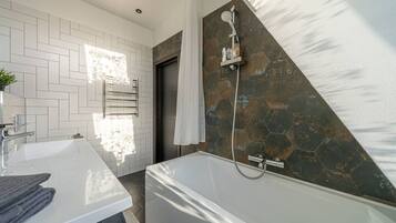 A modern bathroom with a white vanity, a bathtub, and a shower area with a stone wall.