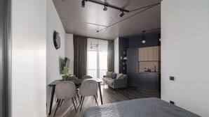 Un dormitorio moderno con una cama grande, un comedor con sillas, una pequeña cocina y un balcón con vistas.