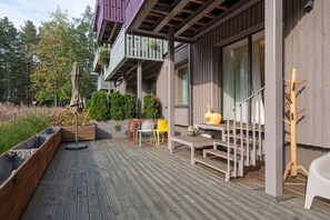 Une terrasse en bois avec des meubles d’extérieur, un escalier et un bâtiment doté de balcons.