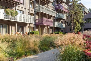 Un immeuble résidentiel à plusieurs étages, doté de balcons, d’une allée pavée et entouré de végétation.