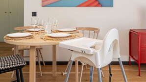 Zona pranzo con tavolo in legno apparecchiato per quattro persone, una sedia bianca e una lampada a sospensione gialla.
