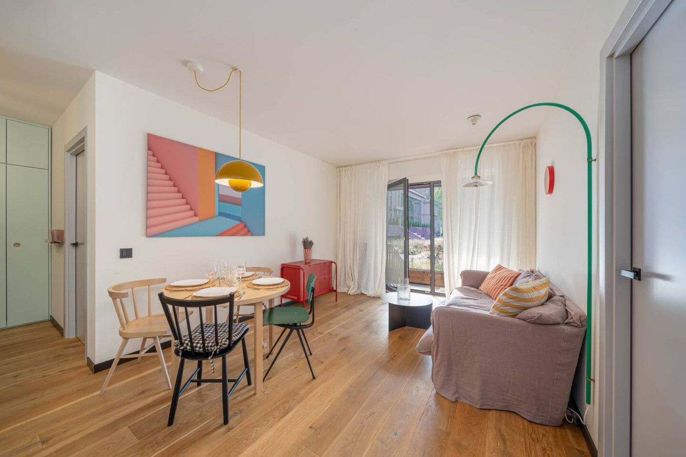 A modern living room with a dining area, a staircase, and a large window.