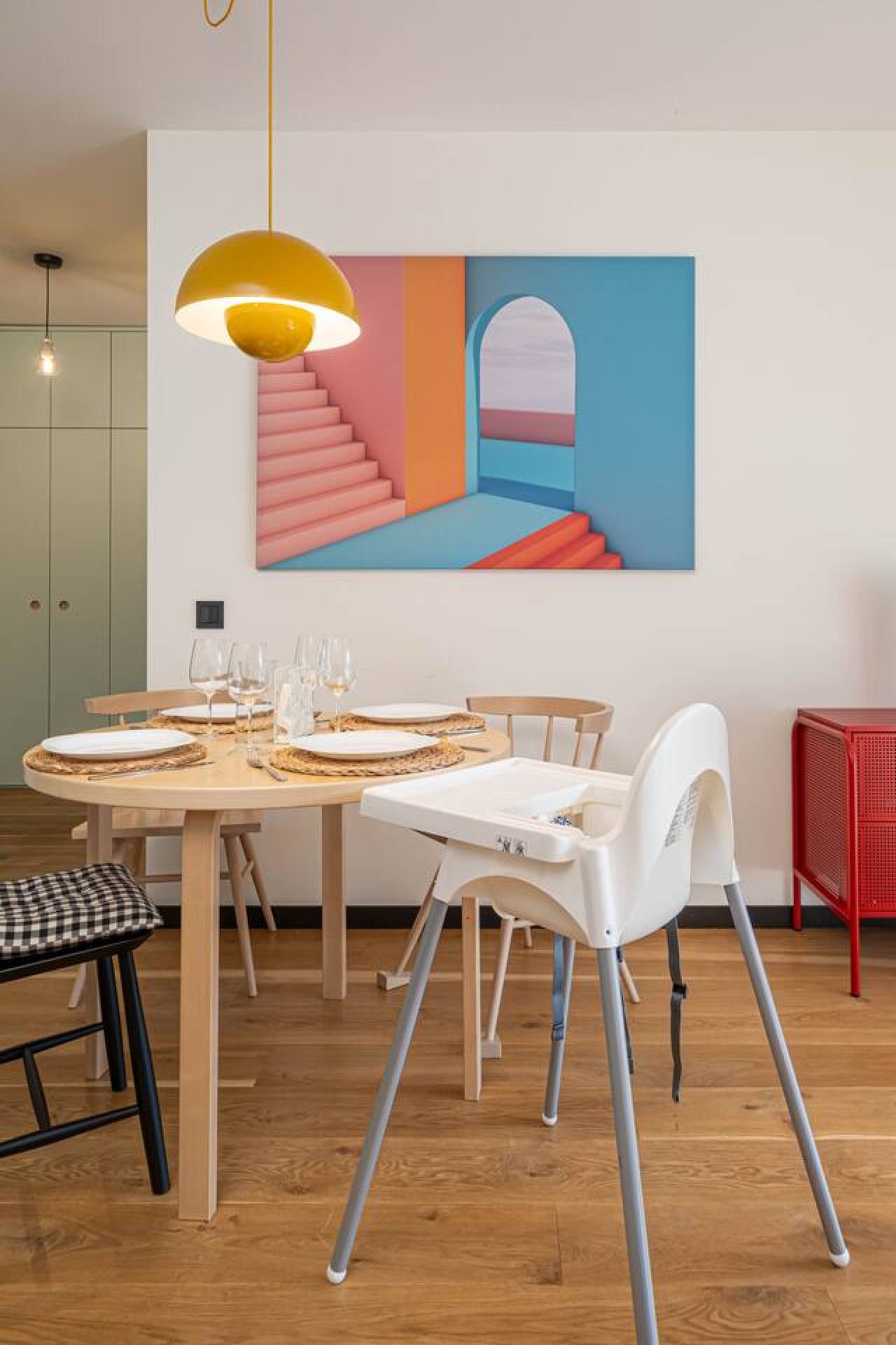 A dining area with a wooden table set for four, a white chair, and a yellow pendant light.