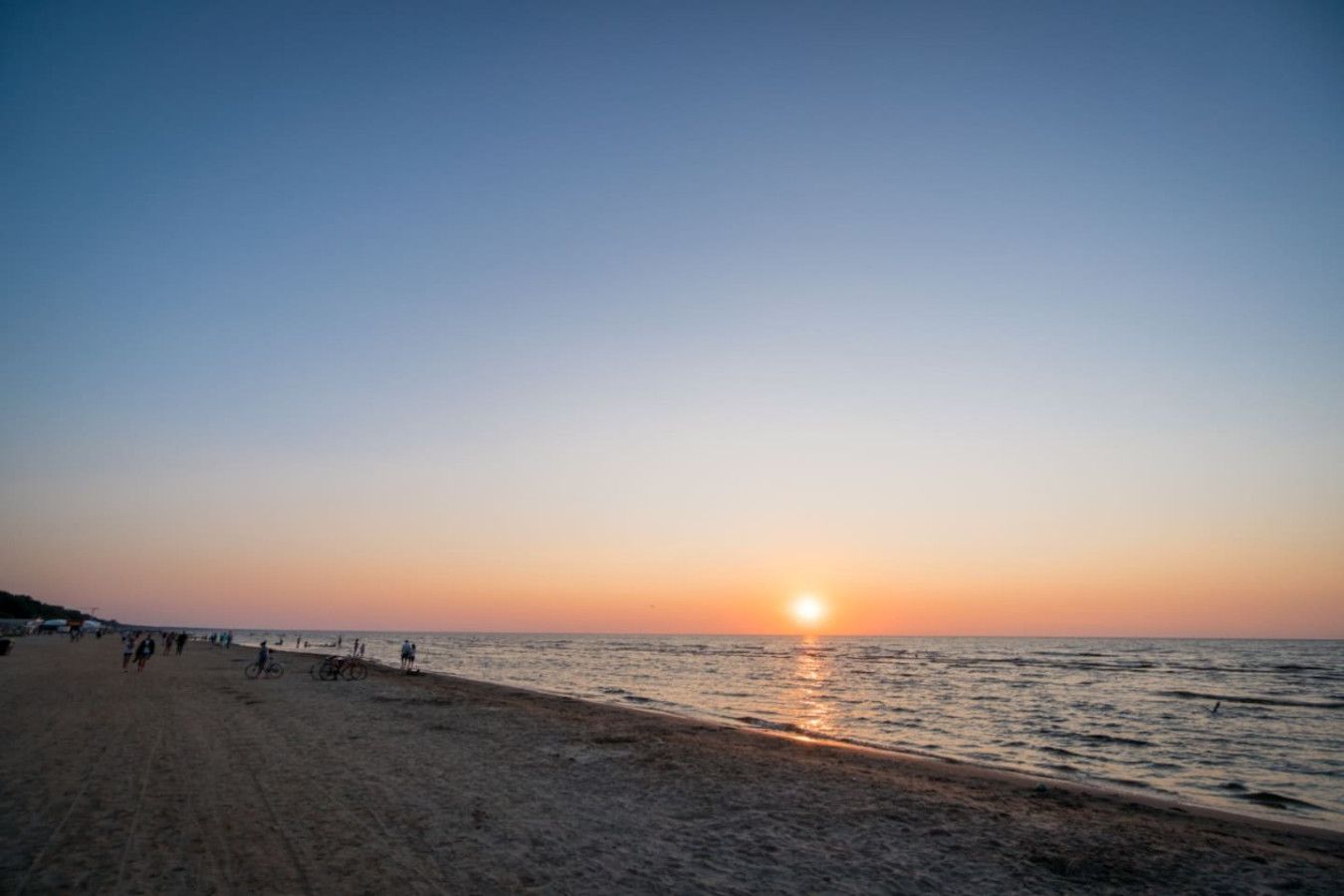A beach at sunset with people walking and a clear sky.