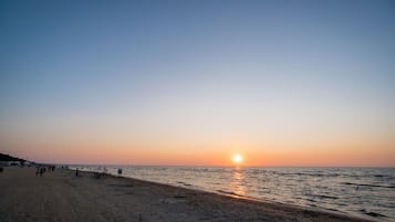 A beach at sunset with people walking and a clear sky.