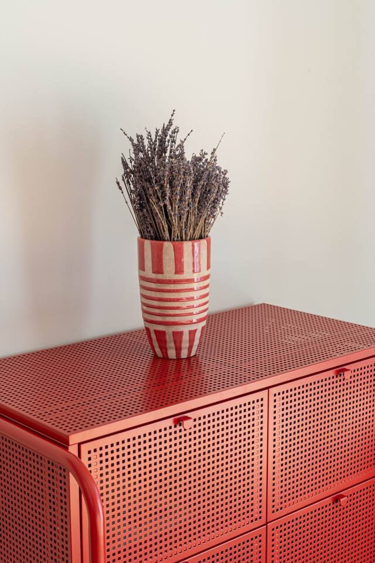 Un mueble metálico rojo con un florero a rayas que contiene lavanda seca.