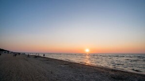 Spiaggia al tramonto con persone che passeggiano e cielo sereno.
