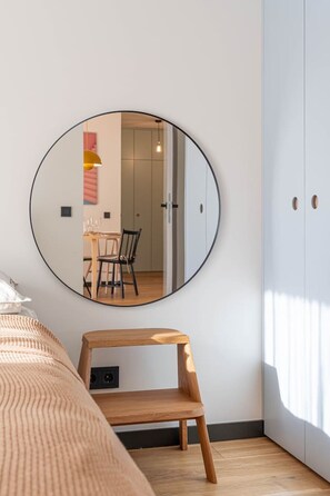 Une chambre à coucher avec un lit, une chaise en bois, un miroir rond et une armoire.