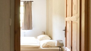 Quarto com cama, mesa de cabeceira com luminária, guarda-roupa de madeira e janela com cortinas.