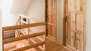 Uma escada de madeira leva a um quarto no sótão com teto inclinado e uma grande janela.