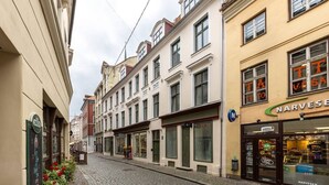 A narrow cobblestone street lined with historic buildings, including a store with a visible sign. - Sojourn in Old Town studio apartment (Riga)