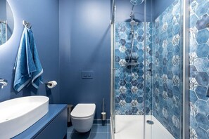 Une salle de bain moderne avec un grand lavabo blanc, des toilettes et une douche en verre, dont le sol est recouvert de carreaux hexagonaux.