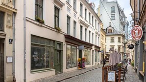 A cobblestone street lined with historic buildings, a street vendor cart, and a clear blue sky. - Romantic studio apartment in Old Town Riga (Rīga)
