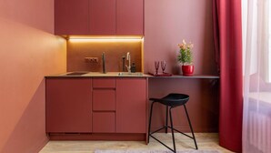 A compact kitchen with a red color scheme, a sink, a bar stool, and a potted plant. - Romantic studio apartment in Old Town Riga (Rīga)