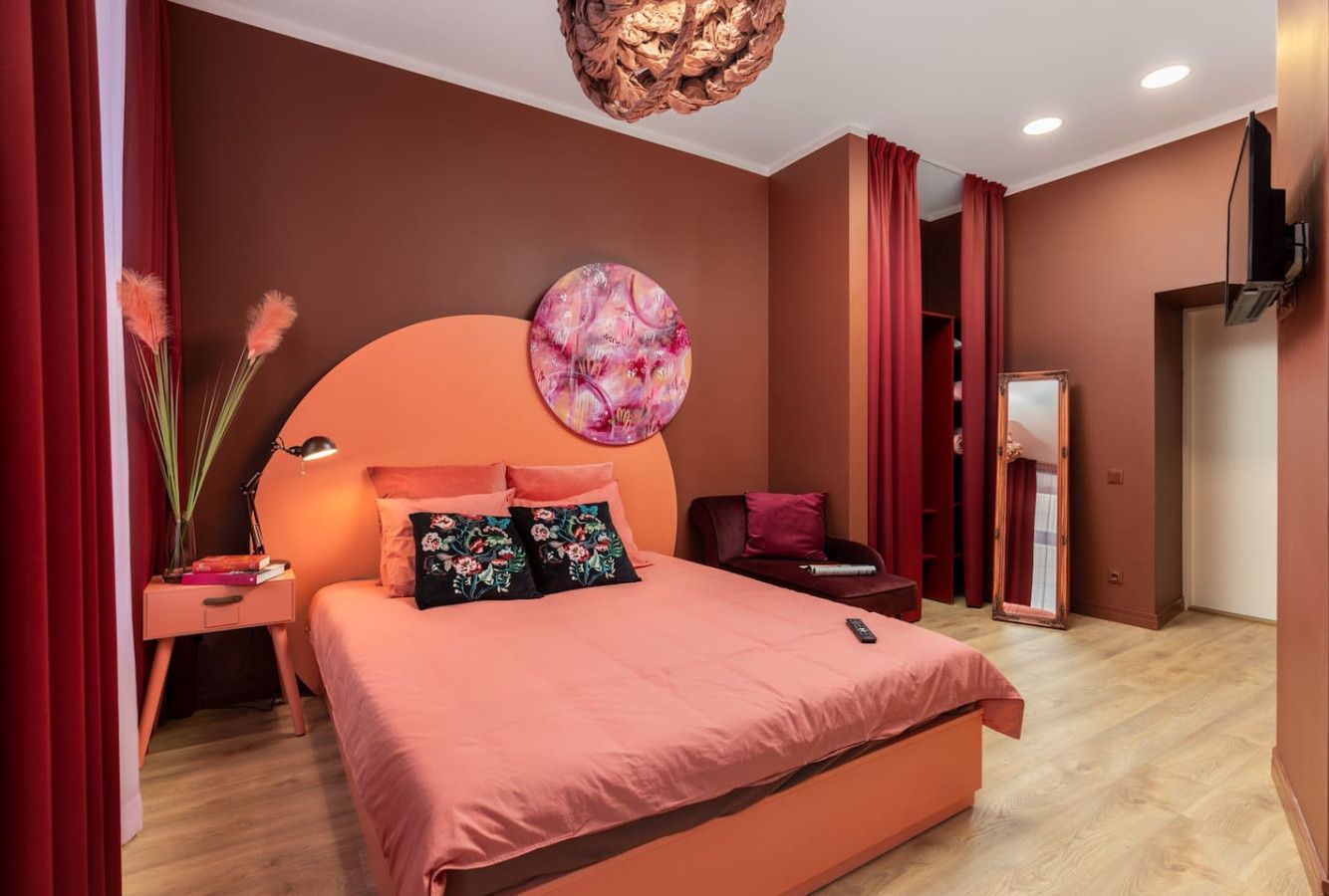 Un dormitorio con una cama grande, una mesita de noche, un televisor montado en la pared y un espejo.