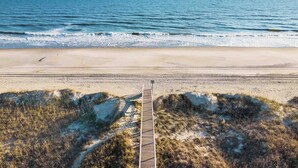 A beach with a wooden boardwalk leading to the water, surrounded by dunes and sparse vegetation. - Sonrise 5-bedroom, 5.5-bathroom home w/ private pool, ~4 mins to the beach! (Ocean Isle Beach)