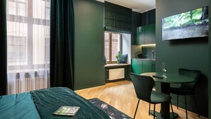 Una habitación moderna con cama, escritorio, silla, una mesita con un vaso y televisor en la pared.