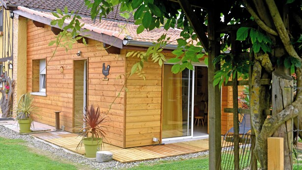 A wooden cabin with a tiled roof, a glass door, and a small deck area.
