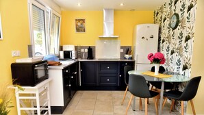 A compact kitchen with a microwave, toaster, and coffee maker on the counter, a dining table with chairs, and a refrigerator.
