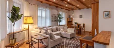 A cozy living room with a wooden ceiling, a large sofa set, a dining table, and a patterned rug.
