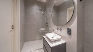 A modern bathroom with a walk-in shower, a large mirror, and a white sink.