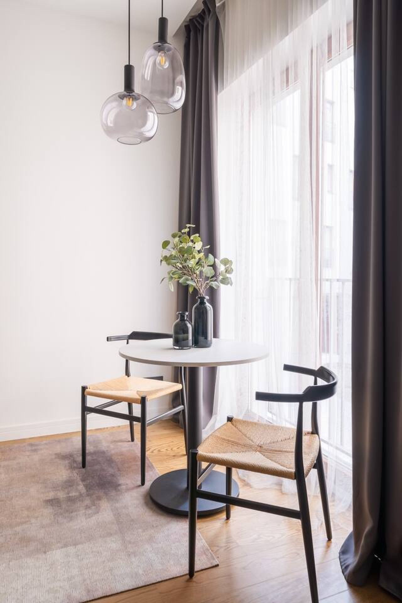 Un área de comedor moderna con una mesa redonda, dos sillas y lámparas colgantes.