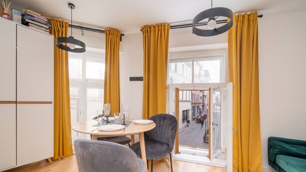 Uma sala de estar moderna com área de jantar, um sofá verde e vista para a rua através de janelas amplas.