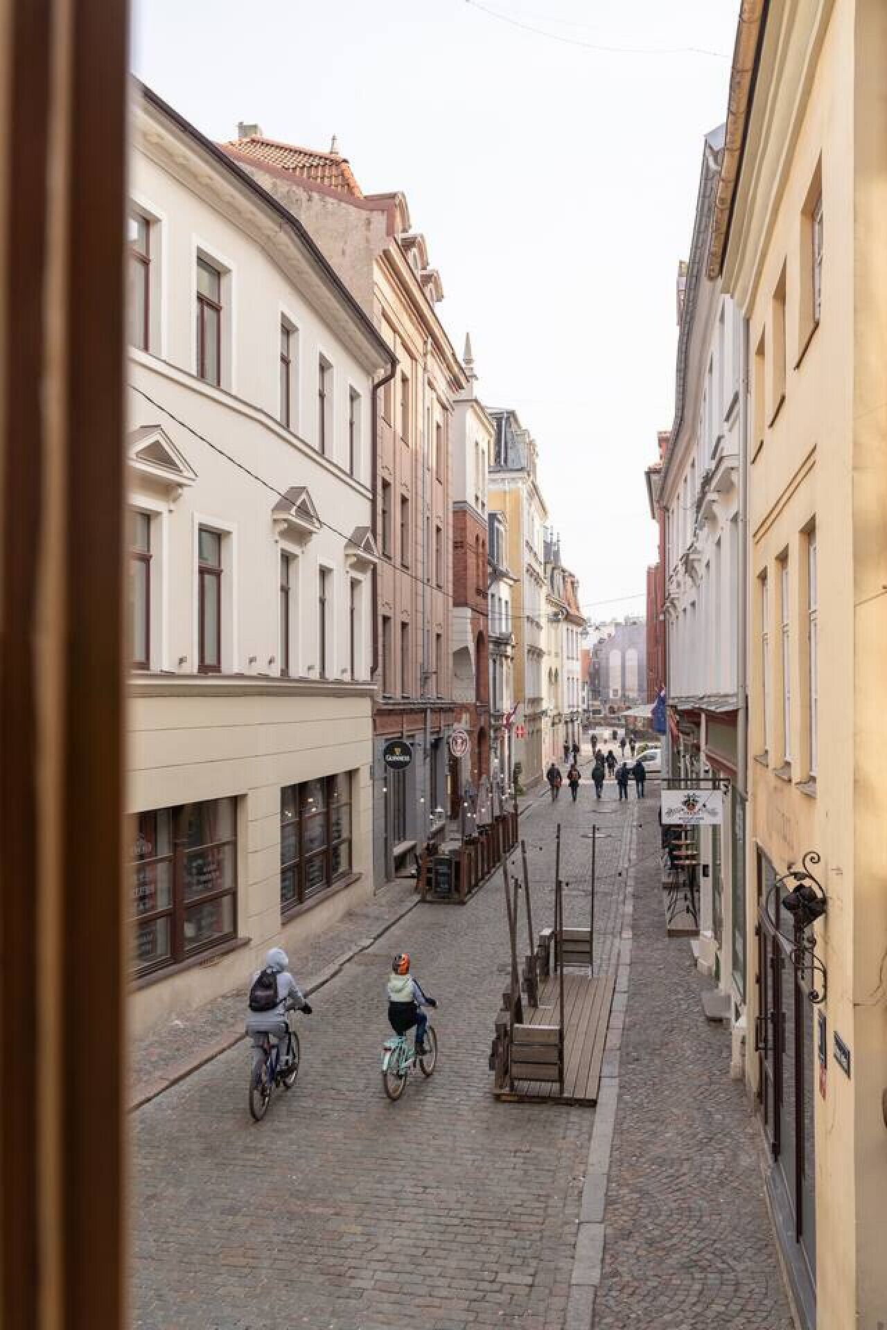Eine Kopfsteinpflasterstraße gesäumt von historischen Gebäuden und schmalen Bürgersteigen, mit einigen Radfahrern.