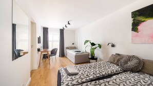 Quarto moderno com cama grande, escrivaninha e cadeira. Há uma planta na escrivaninha e um quadro na parede.