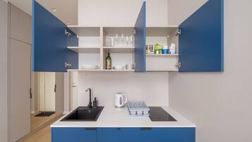 Een koelkast, een kookplaat, kookgerei, borden en bestek, eettafels