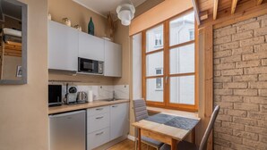 Una cuina compacta amb microones, cafetera i un rentapeus. Hi ha una finestra amb vistes a un edifici de maó i una taula amb cadires.