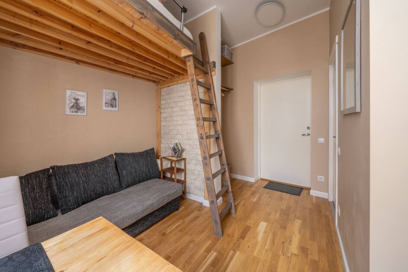 A cozy room with a wooden ceiling, a gray sofa, a wooden ladder, and a white door.