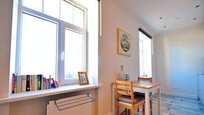 Une pièce lumineuse avec une grande fenêtre, une table en bois entourée de chaises et un radiateur placé sous la fenêtre.