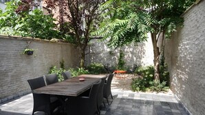 A patio with a wooden table and wicker chairs, surrounded by a brick wall and greenery. - Charming House in Ghent (Gent)