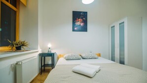 Ein Schlafzimmer mit einem Bett, einem Nachttisch, einem Heizkörper, einem Fenster mit einer Pflanze und einem Bild an der Wand.
