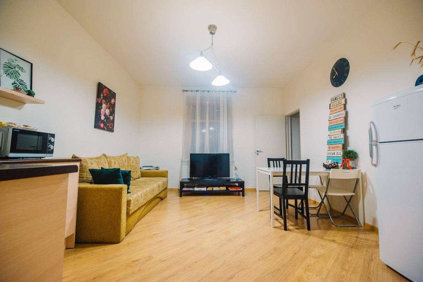 A compact living space with a sofa, TV, dining table, chairs, and a refrigerator.