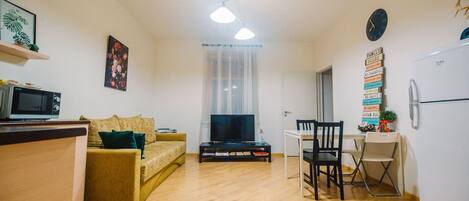 A compact living space with a sofa, TV, dining table, chairs, and a refrigerator.